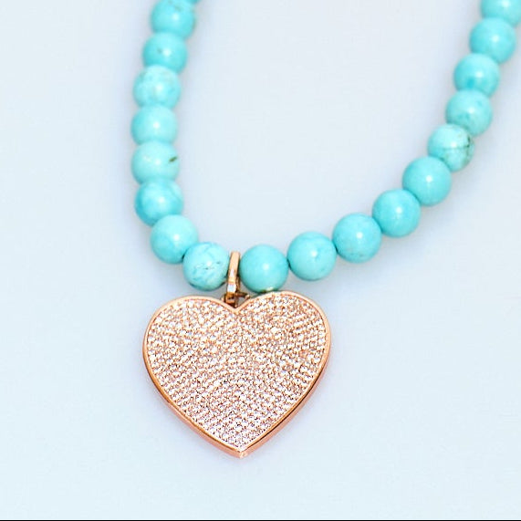 Turquoise beaded necklace with a heart-shaped pendant on a light blue background